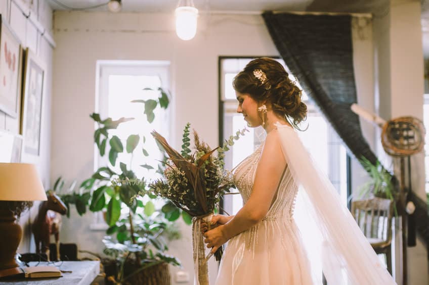 beautiful caucasian young bride uropean in white wedding dress in boho style posing near window while waiting for the groom on wedding day. beautiful bride style. wedding day, happiness, stylish